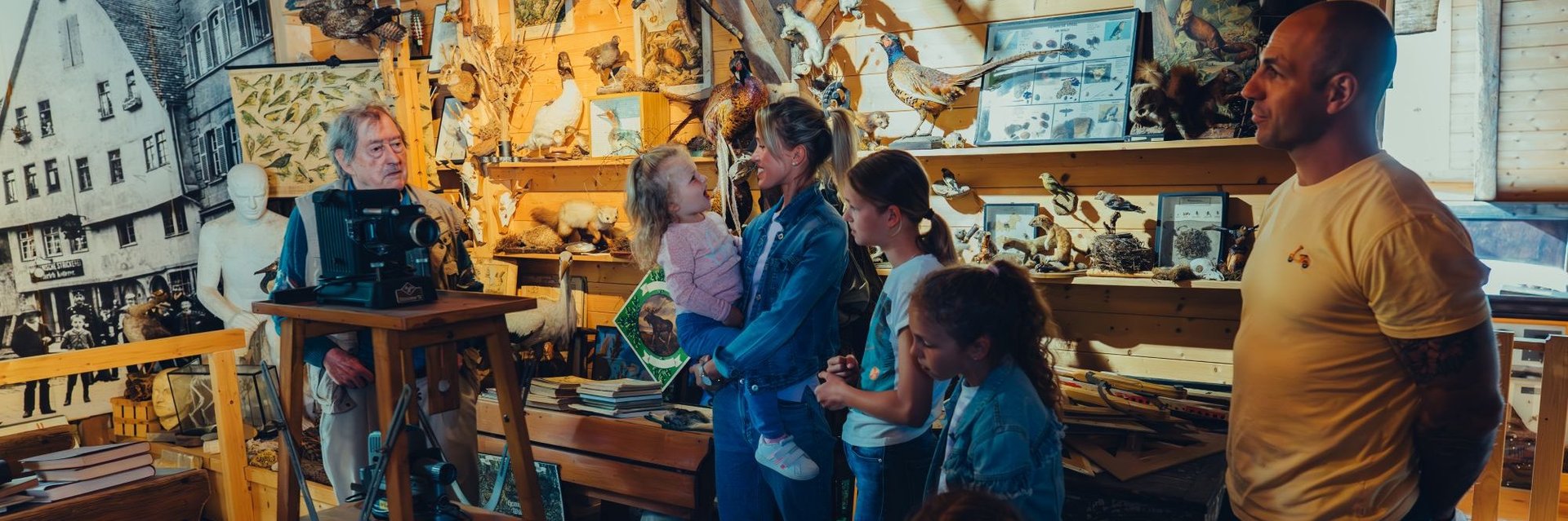 Mehrere Personen unterschiedlichen Alters stehen in einem Museum mit zahlreichen ausgestellten Vogelfiguren und Bildern an den Wänden