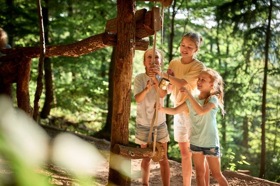 Drei Mädchen spielen an einer Kugelbahn im Wald.