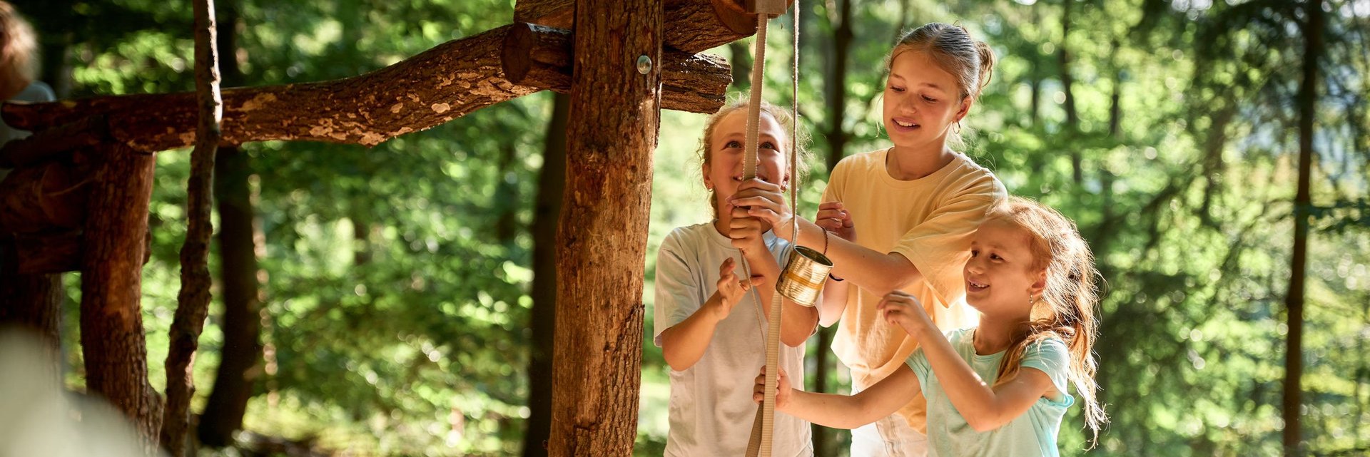 Drei Mädchen spielen an einer Kugelbahn im Wald.