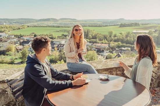 Drei Personen sitzen am Tisch, trinken Kaffee und genießen die Aussicht