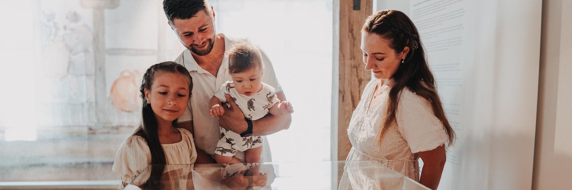 Familie mit zwei Kindern betrachtet Ausstellungsstücke in einem Museumsvitrinenschrank. 