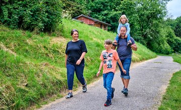 Familie läuft auf einem befestigten Weg neben grünen Hügeln